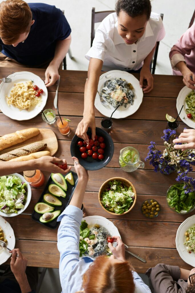 A group of people sharing a vibrant meal with salads, pasta, and fresh vegetables, promoting togetherness.