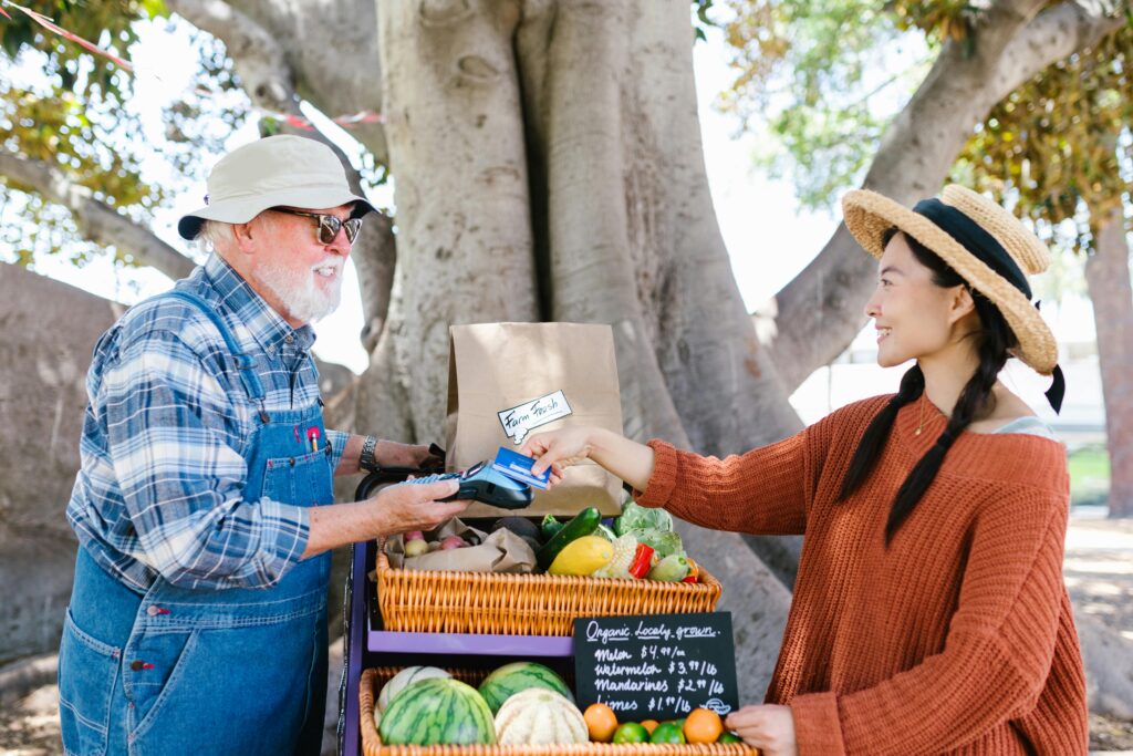 A cheerful exchange at an outdoor farmer's market with fresh produce displayed.